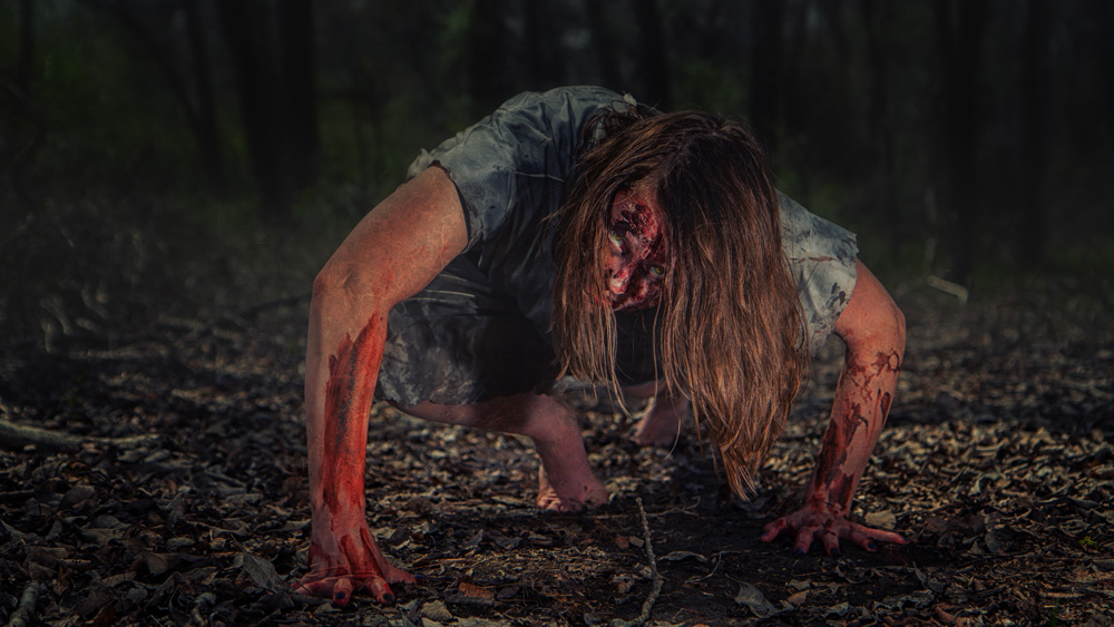 A woman crawling on the ground, covered in blood